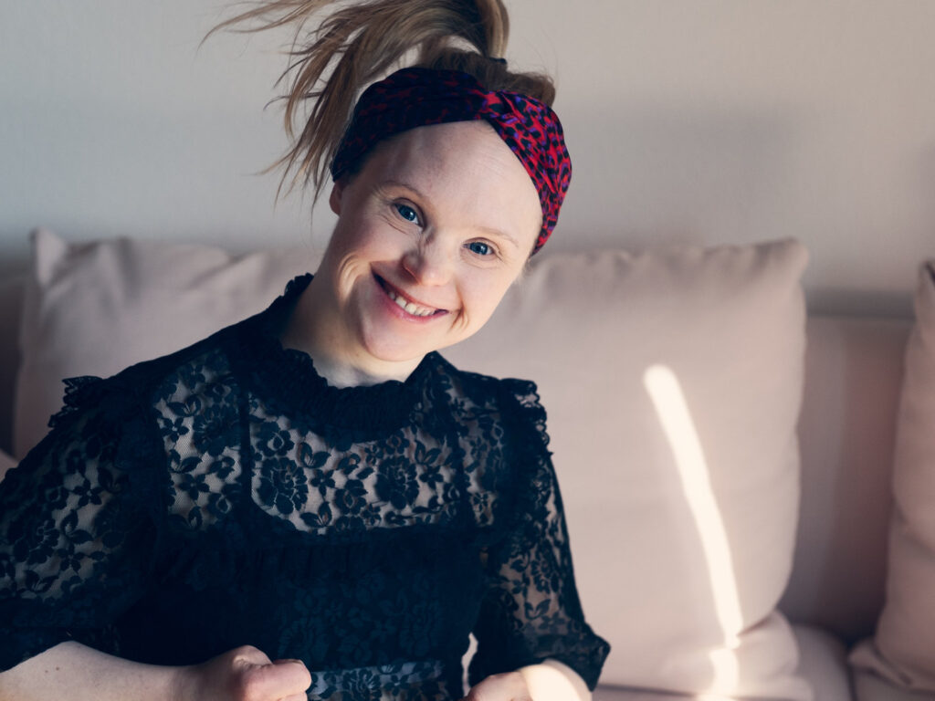 Neele Buchholz sitzt lachend auf einem Sofa und trägt ein rotes Haarband.